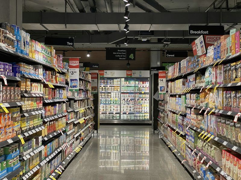 A bright grocery aisle leading to refrigerated cases