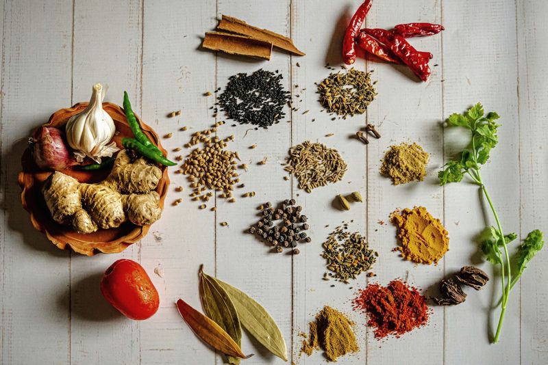 Whole and ground spices, chiles, garlic and herbs arranged on a light surface